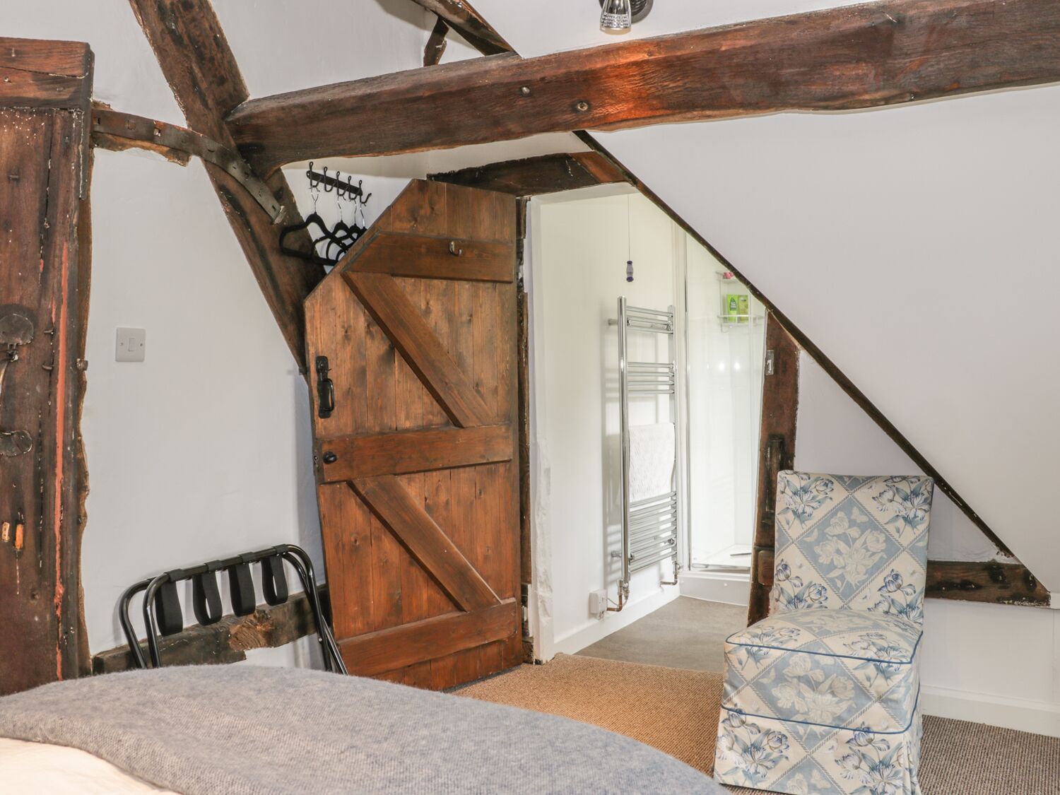 Ein Schlafzimmer mit Holztür, einem Bett, einem Stuhl und Blick auf ein Badezimmer.