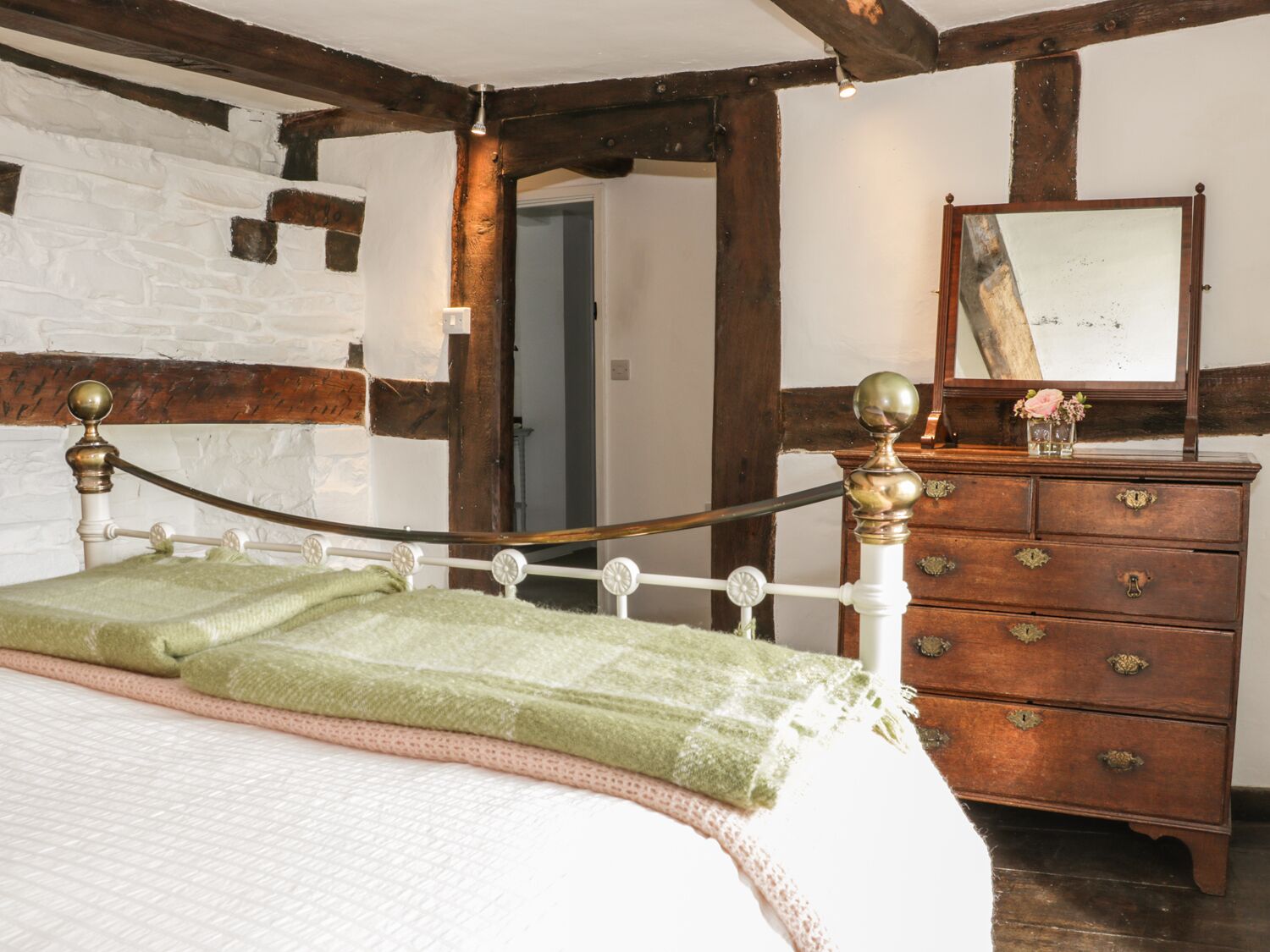 Een kamer met een bed, een houten dressoir en een spiegel.