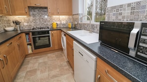 A modern kitchen with wooden cabinets, a dishwasher, a stove, and a microwave. - 12 Kel Avon (Truro)