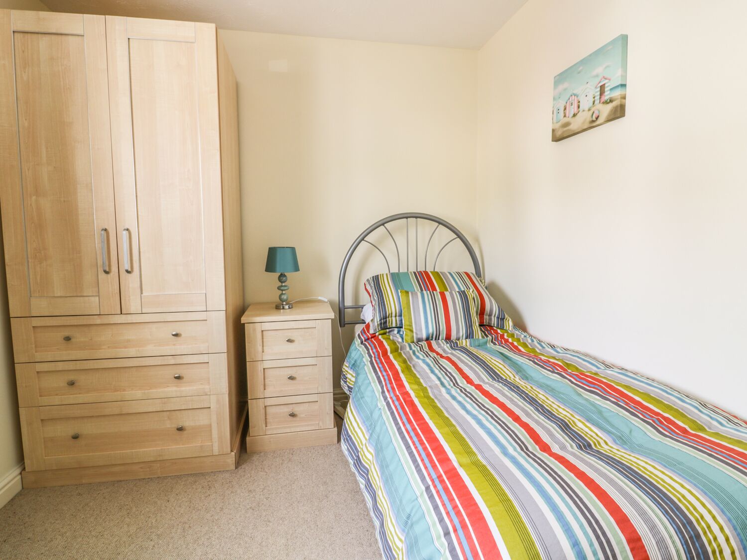 A bedroom with a bed, a nightstand, a lamp, a wardrobe, and a painting on the wall.
