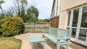 A patio with a wooden bench and a table, surrounded by a garden and a wooden fence. - 12 Kel Avon (Truro)
