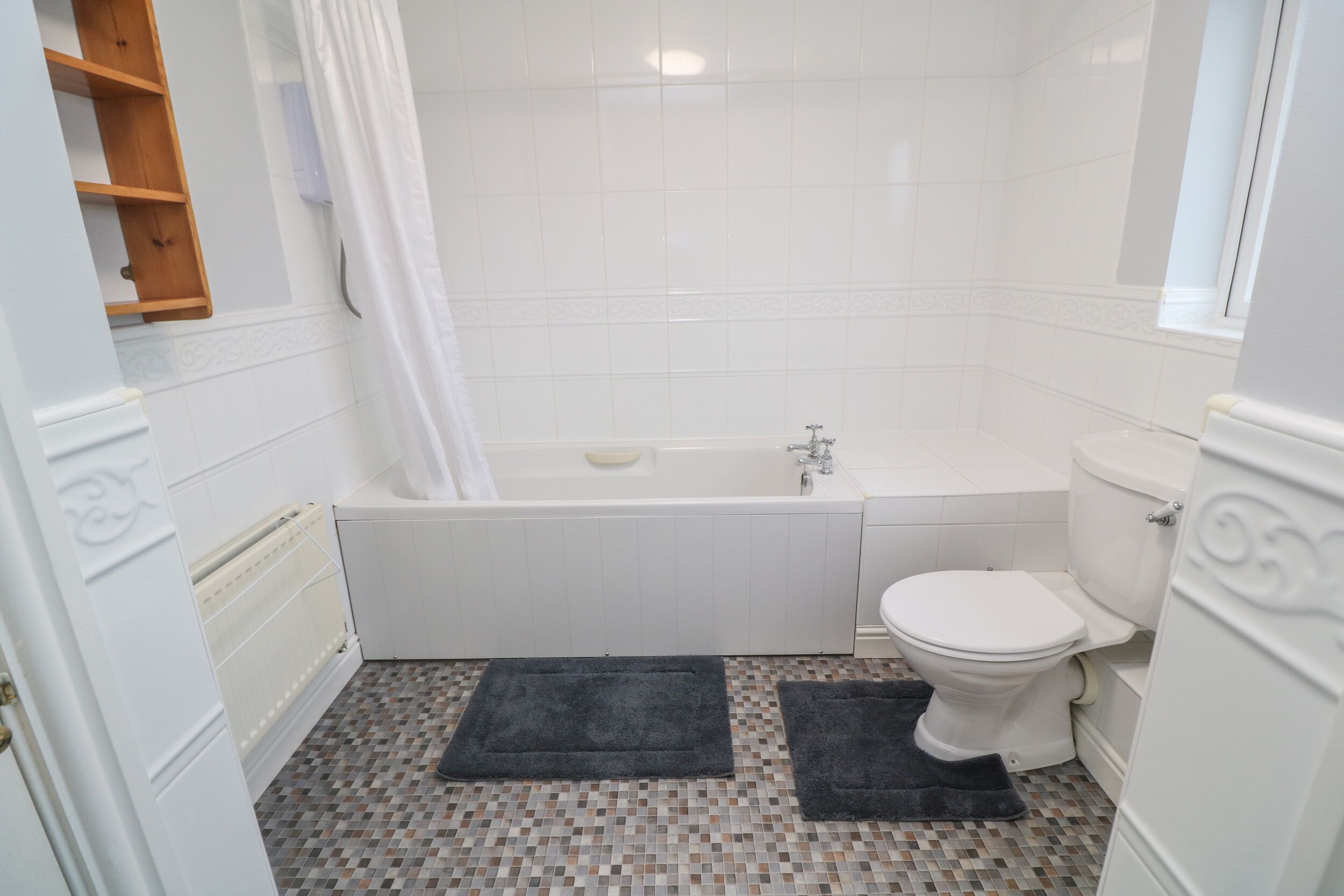 A bathroom with a bathtub, toilet, and a shower curtain. There are two dark mats on the floor.