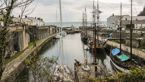 A harbor with several sailboats docked, a stone wall, and buildings in the background. - Oh Buoy! (St Austell)