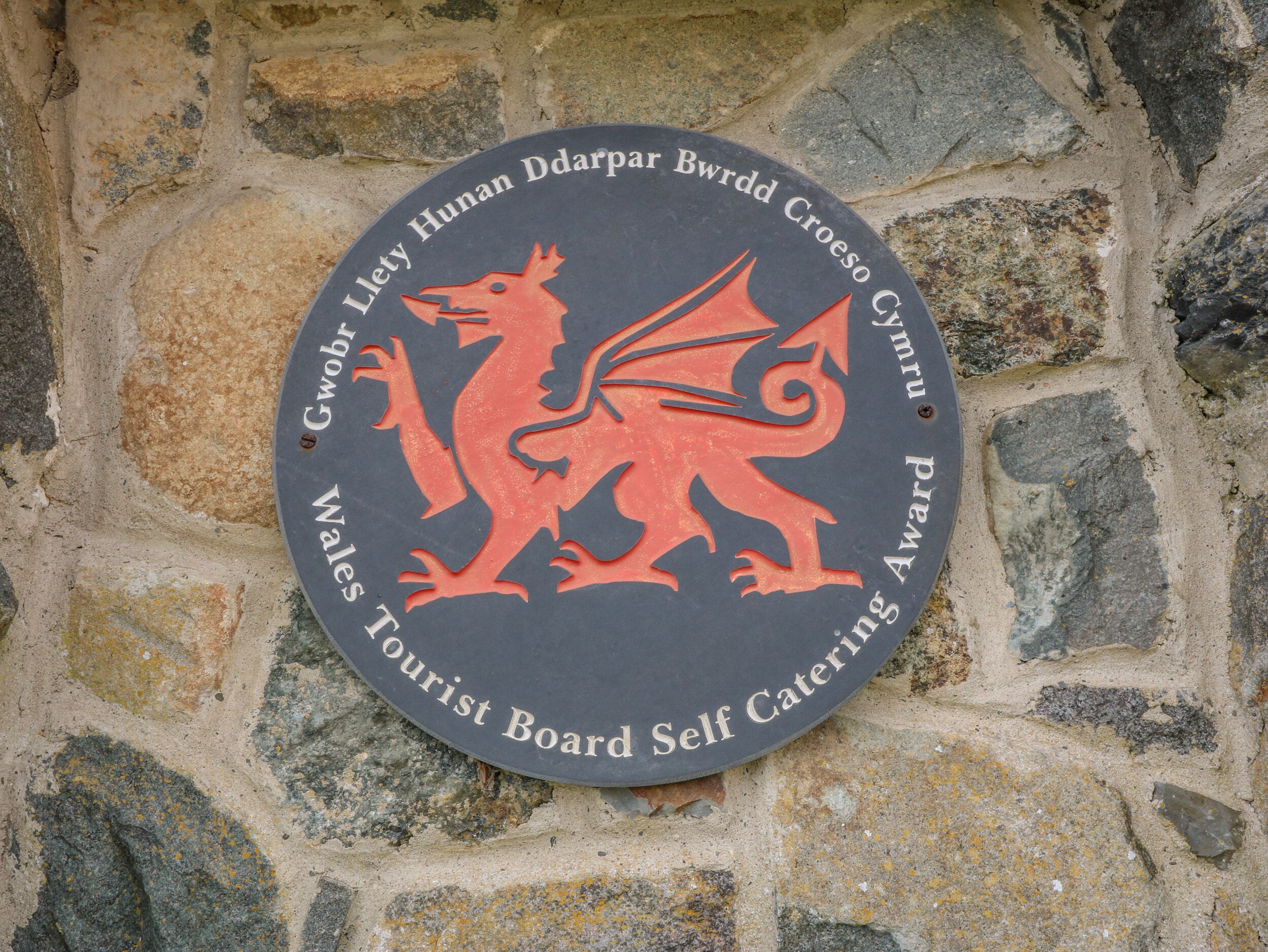 Eine runde Plakette mit einem roten Drachenwappen und dem Hinweis, dass es sich um eine Auszeichnung der Wales Tourist Board für Ferienwohnungen handelt.