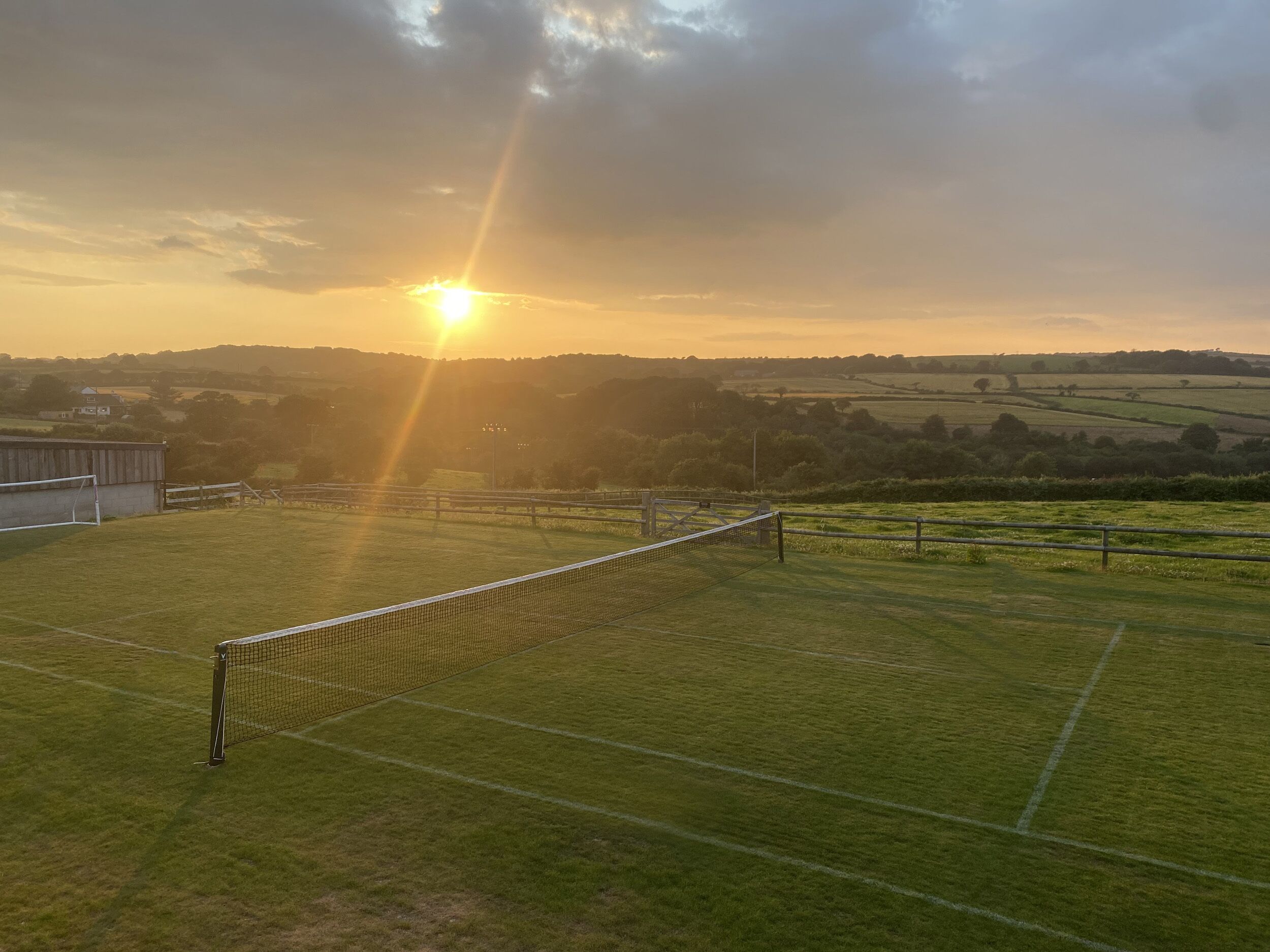 Un campo da tennis con una rete in primo piano e un tramonto sullo sfondo.