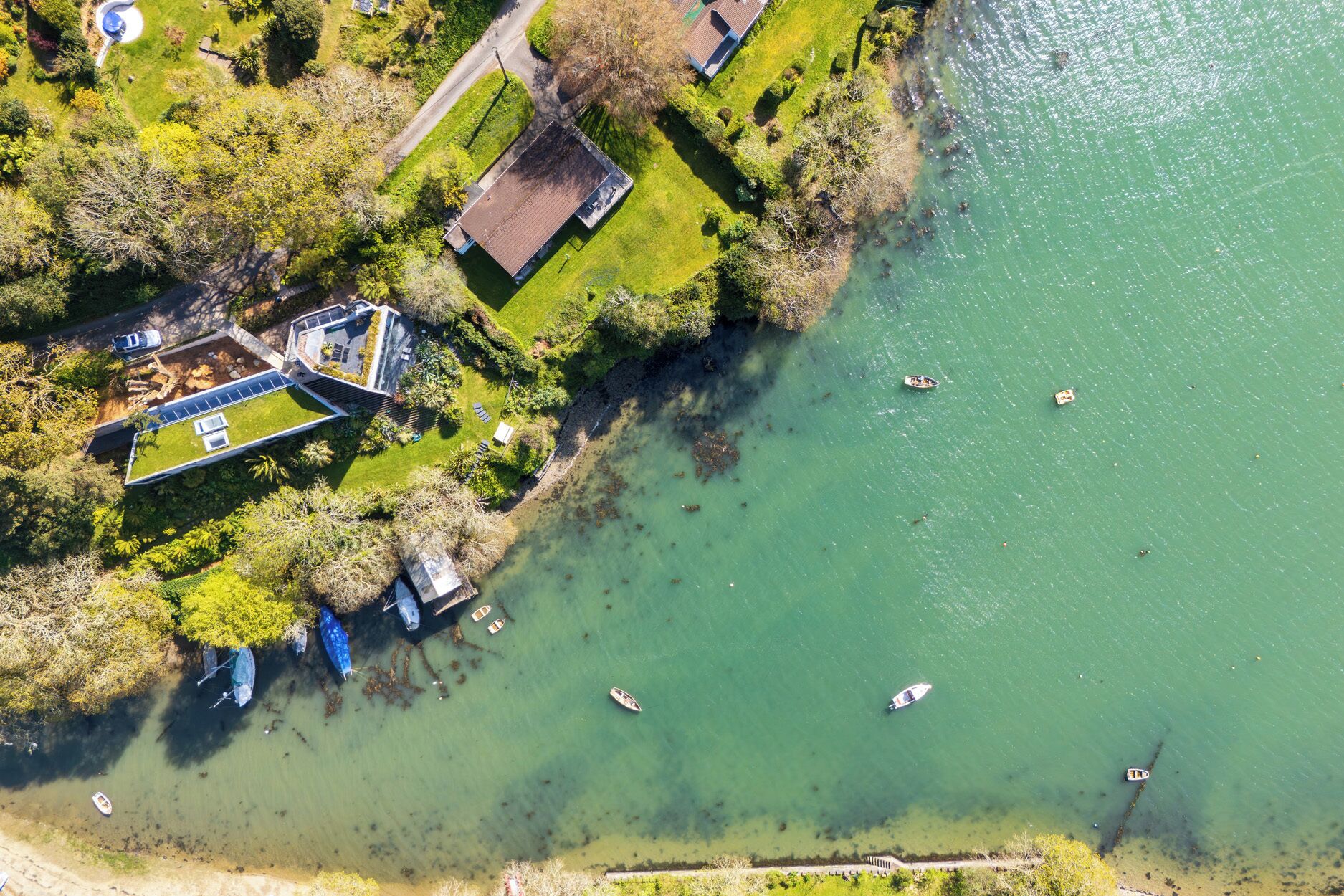 Luchtbeeld van een landgoed aan het meer, met een huis, een steiger voor boten en omliggende begroeiing.