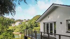 Un bâtiment blanc doté d’un balcon, avec une rivière et une végétation luxuriante tout autour.