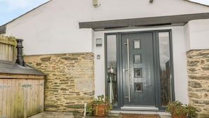 A building with a stone exterior, a grey door with a glass panel, and two potted plants on the porch. - The Bolthole (Newquay)