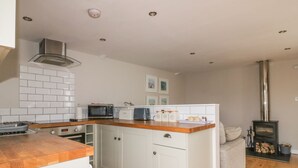 A compact kitchen with white cabinetry, a wooden countertop, a built-in microwave, and a wood-burning stove. - The Bolthole (Newquay)