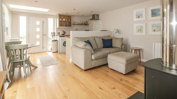 A spacious living area with a sofa, a dining table, and a kitchen in the background. - The Bolthole (Newquay)