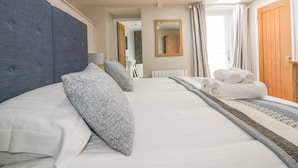 A hotel room with a large bed, a headboard, a bathroom visible through an open door, and a window with curtains. - The Bolthole (Newquay)