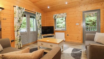 A wooden cabin interior with a sofa, a television, and a window with a view of greenery.