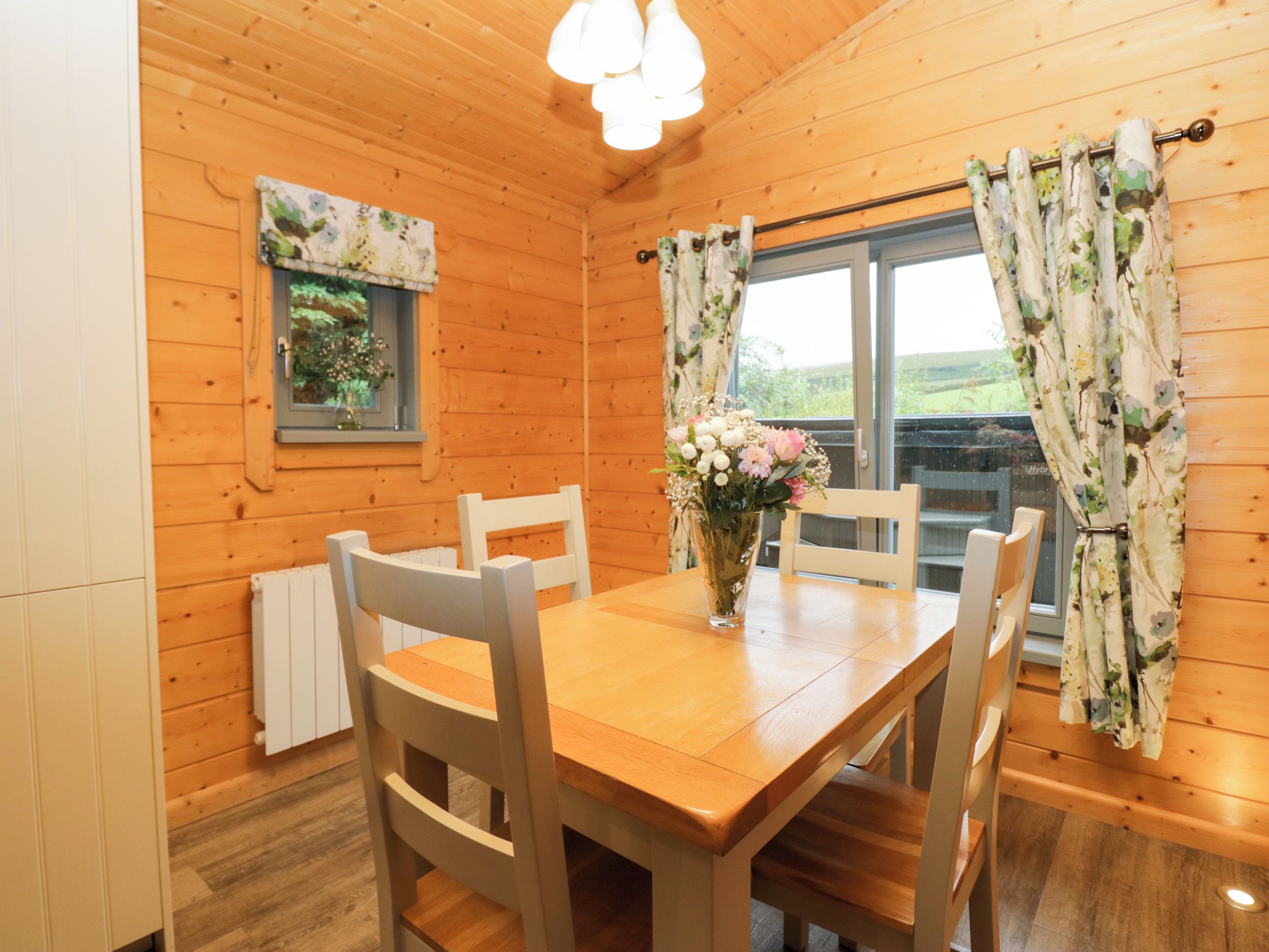 Un intérieur en bois comprenant une table à manger, des chaises, un vase avec des fleurs et des rideaux.