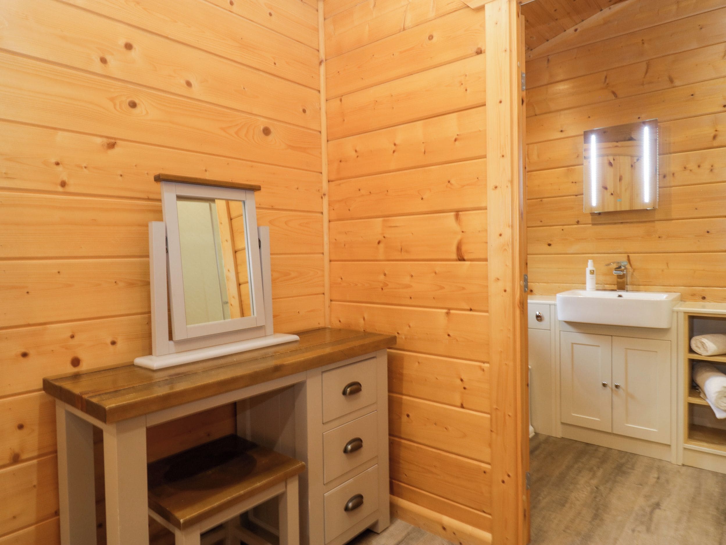 A wooden cabin interior with a wooden desk, a mirror, a white sink, and a cabinet.