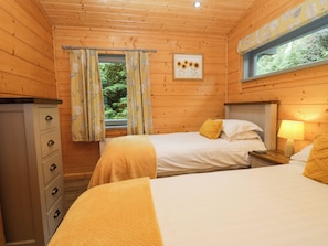 Ein Holzhütten-Zimmer mit zwei Betten, einem Schminktisch, einem Fenster mit Vorhängen und einem Bild an der Wand.