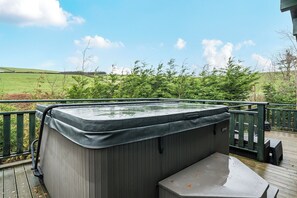 A hot tub on a wooden deck with a view of a green field and trees. - Elm Lodge (Ulverston)