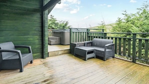 Une terrasse en bois avec des meubles d’extérieur, notamment deux chaises et un canapé, ainsi qu’un jacuzzi.