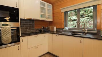 A modern kitchen with wooden cabinets, a black countertop, a stainless steel oven, and a window with a view of greenery.