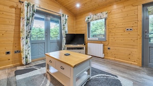 Une pièce de cabane en bois équipée d’une télévision, d’une petite table et de deux fenêtres avec des rideaux.
