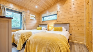 Une chambre rustique en bois avec deux lits, chacun agrémenté de draps jaunes, une fenêtre donnant sur la forêt et un plafond en bois.