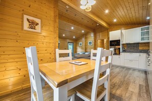 A wooden cabin interior with a dining area, kitchen, and a cozy living space. - Elm Lodge (Ulverston)
