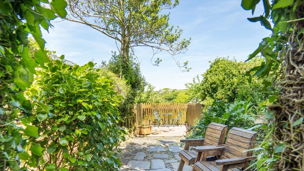 A garden patio with stone flooring, wooden furniture, and a wooden fence in the background.