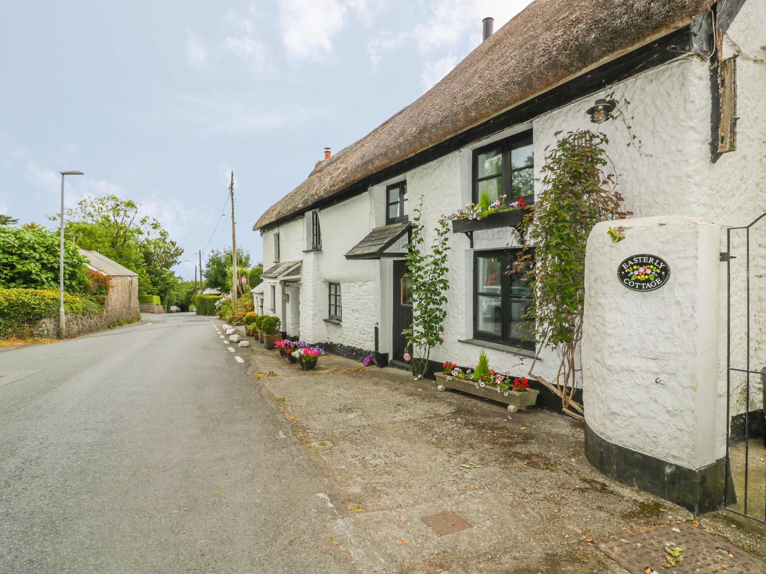 A row of white buildings with thatched roofs, a sign reading "Easterly Cottage," and flower boxes along the sidewalk.
