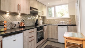 A modern kitchen with wooden cabinets, a built-in oven, a dishwasher, and a window providing natural light.