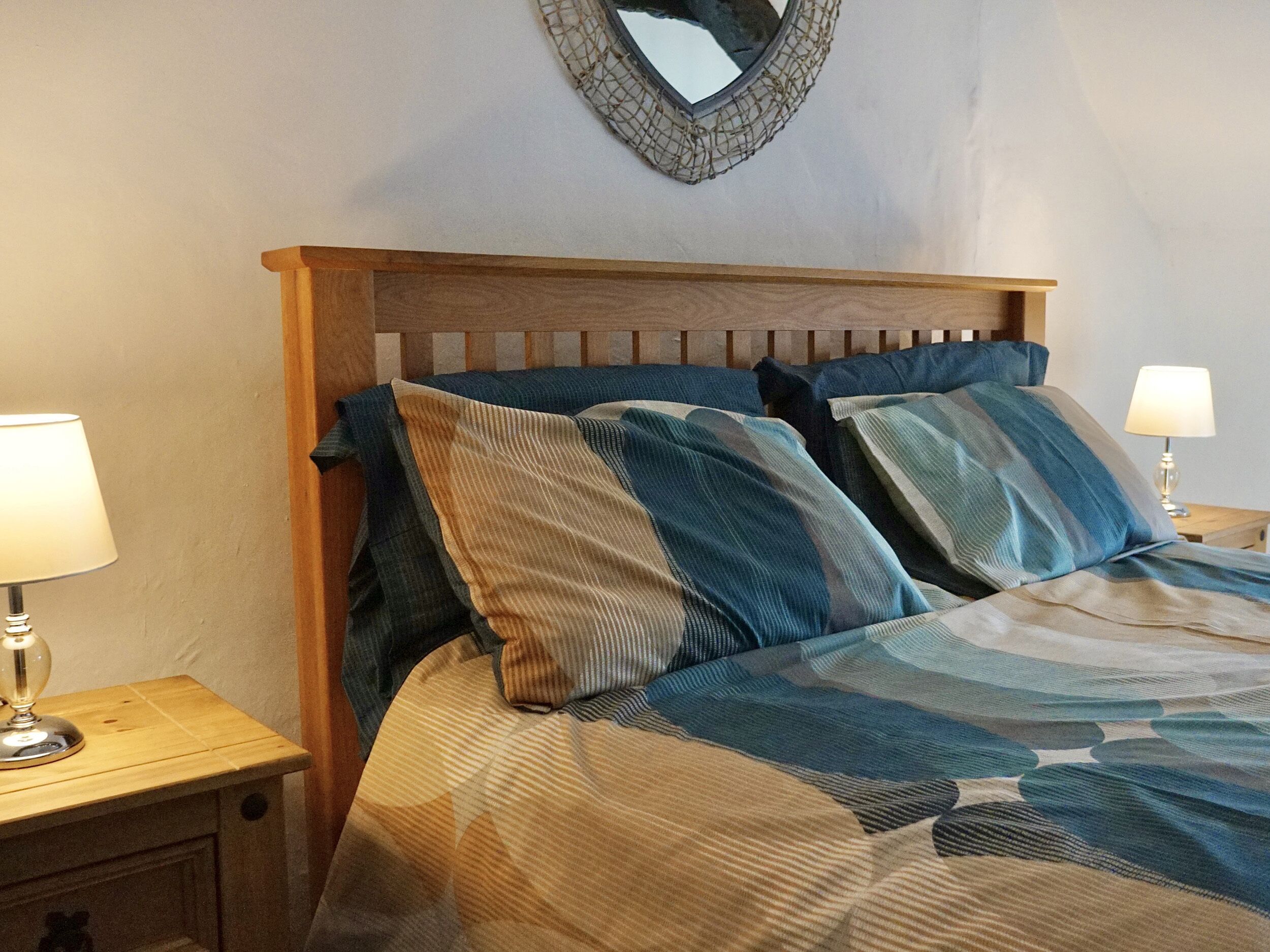 A neatly made bed with a striped blanket, two bedside lamps, and a wooden headboard.