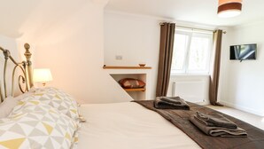 Une chambre à coucher avec un lit, une lampe, un téléviseur et une fenêtre avec des rideaux.