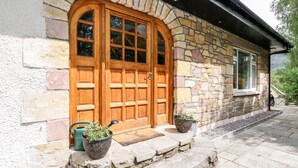 Un bâtiment en pierre avec une grande porte en bois et deux plantes en pot placées sur les marches.