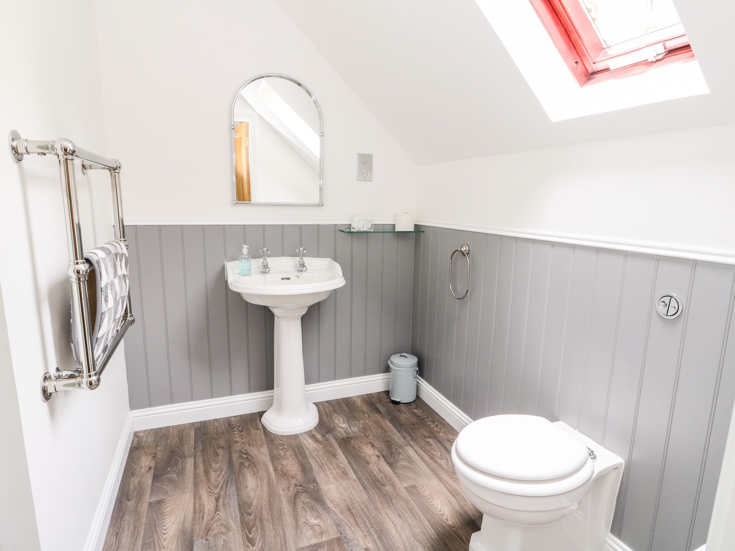 A bathroom with a pedestal sink, a toilet, a towel rack, and a mirror.