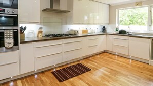 Une cuisine moderne avec des armoires blanches, un four encastré, une cuisinière à gaz et une fenêtre qui laisse entrer la lumière naturelle.