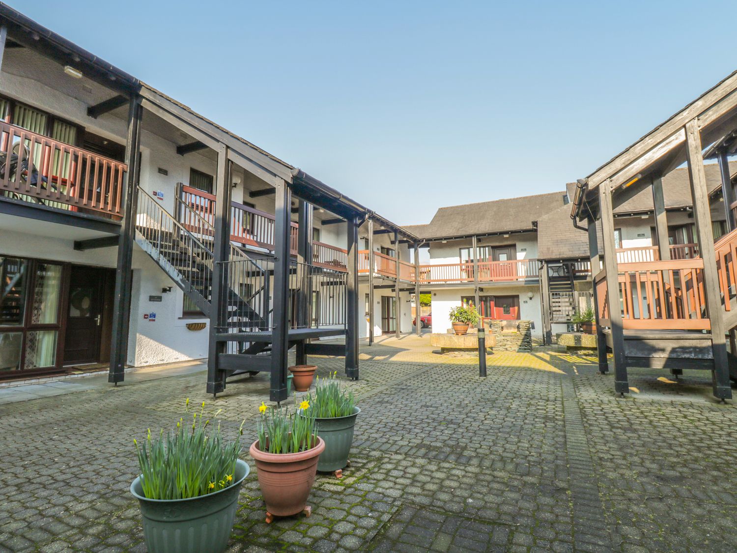 A courtyard with a cobblestone floor, multiple balconies, and potted plants.