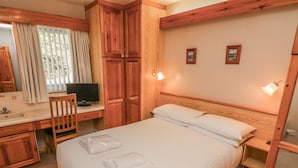 Ett hotellrum med en säng, ett skrivbord med en dator, en stol, en spegel och två väggmonterade lampor.