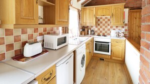 Une cuisine compacte avec des meubles en bois, un four à micro-ondes, un lave-linge et un pare-feu à carreaux.
