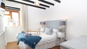 Ett sovrum med en säng, sängbord, en lampa, ett fönster med gardiner och ett element.