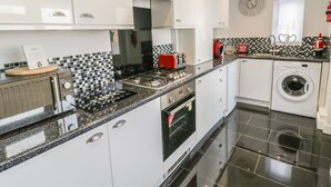 Una cocina moderna con armarios blancos, salpicadero de azulejos blanco y negro, un tostador rojo, una lavadora y un reloj en la pared.