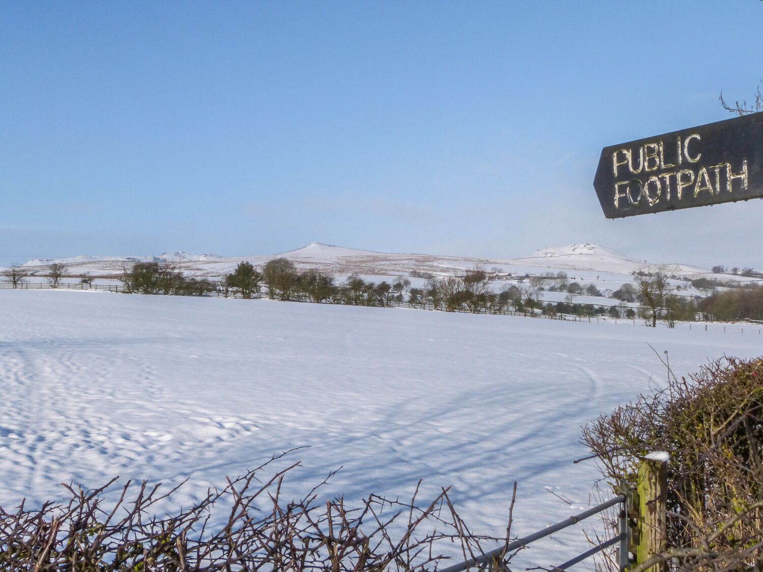 Paisaje nevado con un cartel que indica un sendero público.