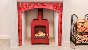 Una estufa de leña roja con un arco de azulejos encima, ubicada en una habitación con paredes blancas y suelo de baldosas.