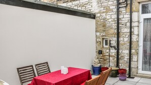 Un patio con una mesa cubierta con mantel rojo, dos sillas de madera y una estatua de Buda.