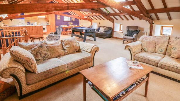 A spacious loft with exposed wooden beams, a pool table, a sofa set, and a dining area.