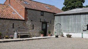 A stone building with a tiled roof, a wooden bench, and potted plants.
