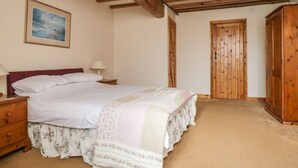 A bedroom with a wooden ceiling, a bed with floral bedding, a nightstand, a lamp, and a wooden wardrobe.