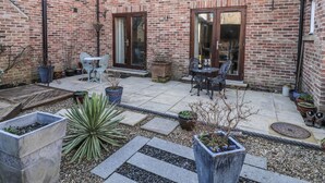 A brick patio with outdoor seating, potted plants, and a small garden area. - Pebble Cottage Dunnscroft (Bridlington)