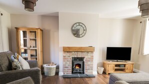 A cozy living room with a fireplace, a television, and a wooden cabinet. - Pebble Cottage Dunnscroft (Bridlington)