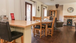 A dining area with a wooden table and chairs, a fireplace, and a kitchen area with a stove. - Pebble Cottage Dunnscroft (Bridlington)