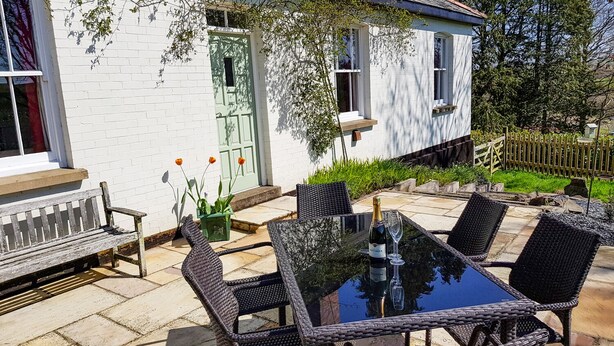 A patio with wicker furniture, a glass table, and a bottle of champagne. - Hedgelea (Okehampton)