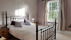 A bedroom with a bed, a nightstand, a window with curtains, and a view of greenery outside. - Hedgelea (Okehampton)
