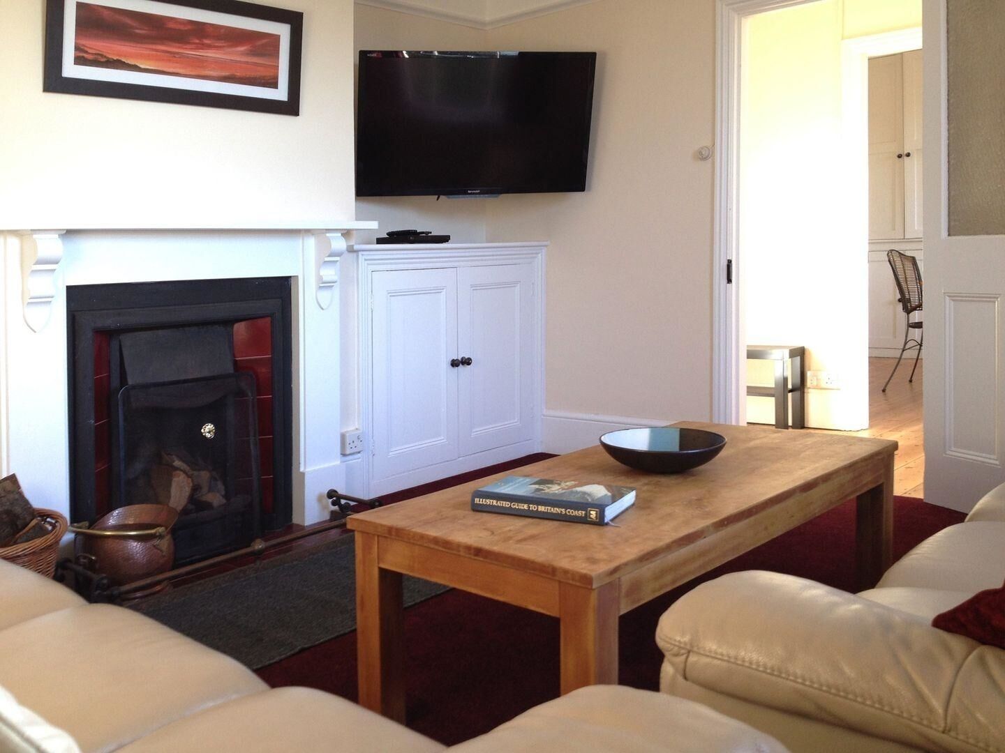 A living room with a fireplace, a television mounted on the wall, a table with a book, and a sofa.